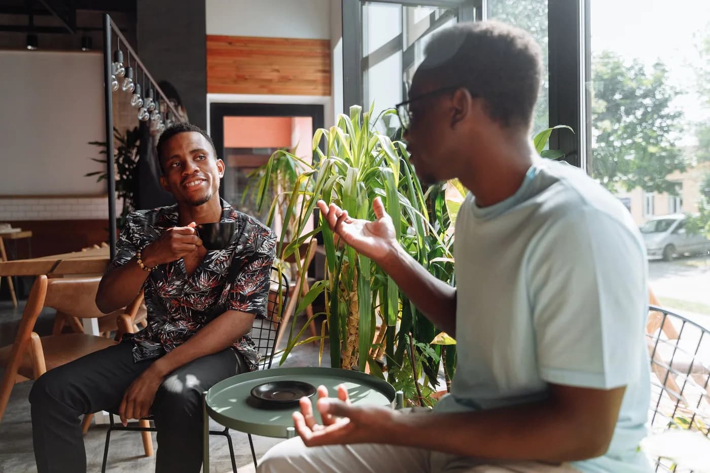 Two friends in a café, one talking with his hands while the other listens