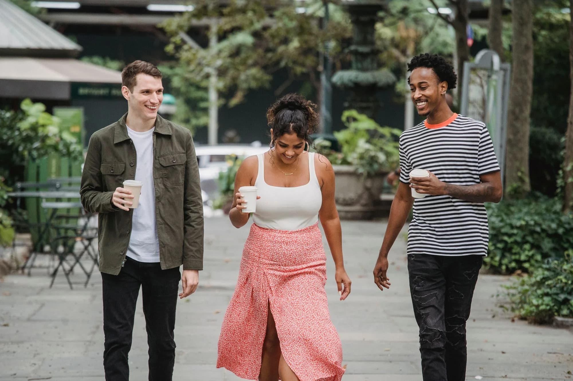 Three friends walking together outside with coffee, talking and laughing